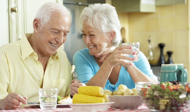 A senior couple eating a meal in a bright kitchen with a large table
